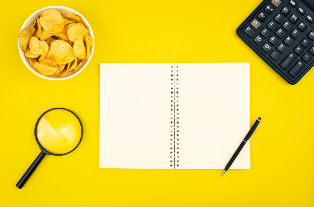 A plate of potato chips, a calculator and a notebook on a yellow background.